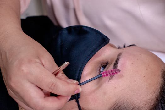 Close-up of a beautician performing eyebrow grooming on a client wearing a mask.